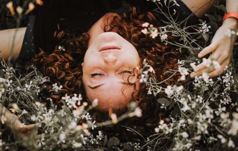 A woman with curly hair, laying in a bed of flowers