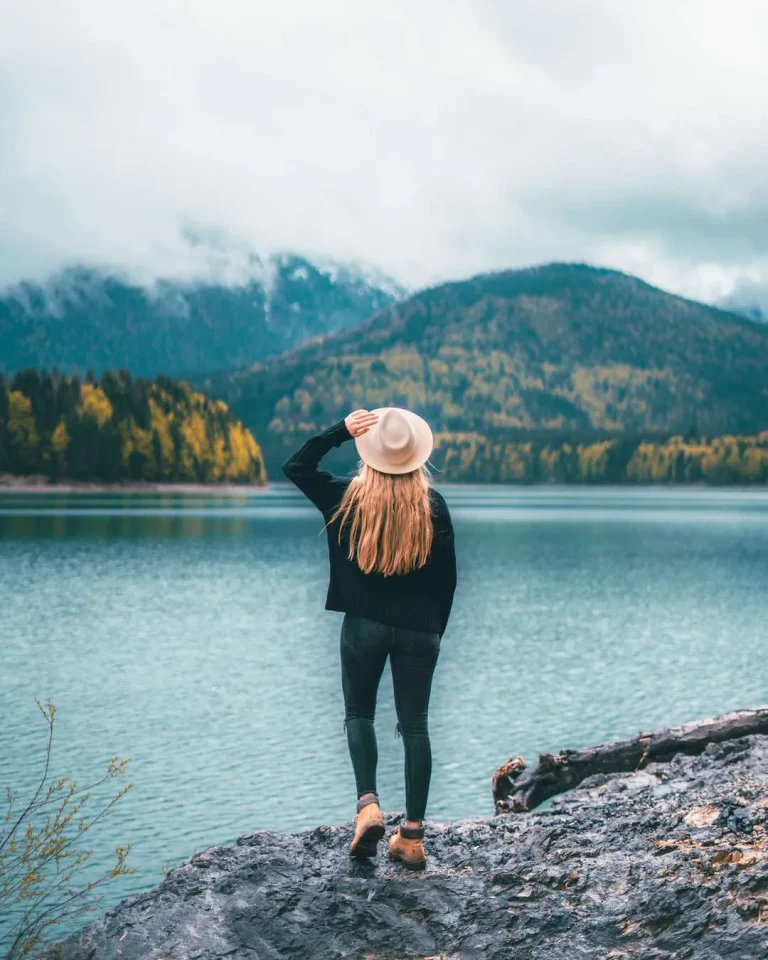 A woman with long blonde hair looking out over a lake with mountains